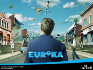 A man stands in a small-town street while people and objects float overhead in a surreal scene.