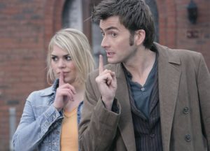 A man and woman hold fingers to their lips in a playful shushing gesture.