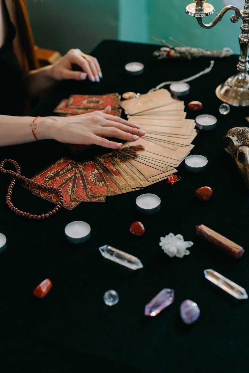 Hands spread tarot cards across a black table surrounded by candles and crystals.