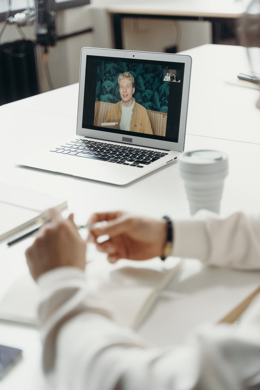 A laptop on a desk shows a man speaking during a video call.